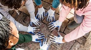 Jóvenes con sus manos con guantes trabajan en un jardín urbano.