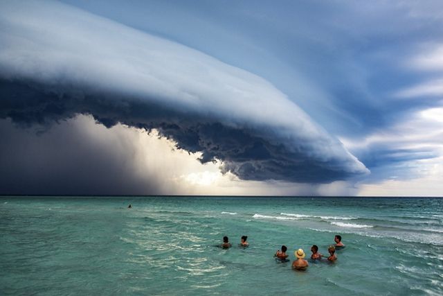 Personas bañándose en el océano turquesa y nubes de tormenta a lo lejos