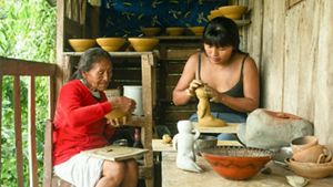 Dos mujeres crean cerámica juntas dentro de una acogedora casa de madera, rodeadas de herramientas y arcilla.