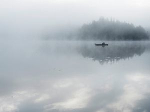 Una persona rema en canoa en un lago brumoso.