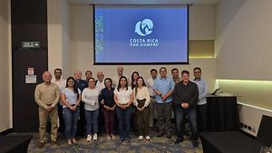 Varias personas posan para foto de grupo con una pantalla en el fondo.