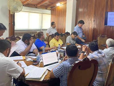 Un grupo de personas sentadas en una mesa presta atención a una pantalla.