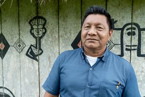 A man in a blue shirt stands in front of a wall adorned with colorful painted designs.