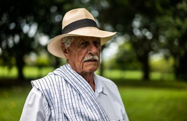 Un hombre mayor con bigote posa con un sombrero de paja.