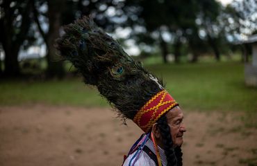 Fotografía de perfil de un hombre mayor con un sombrero de plumas de pavo real.