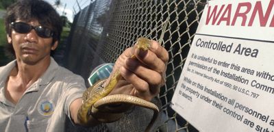 Un hombre sostiene una serpiente frente a un cartel, mostrando su interacción con el animal.