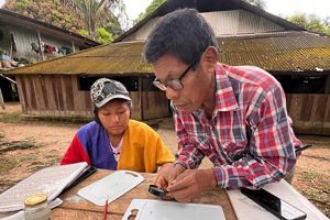 Dos personas indígenas analizando información sobre una mesa de madera.