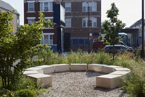 A semi-circle ring of flat, square stones is situated among green plants in a schoolyard. 