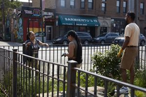 Two people working in a garden chat over a fence with another person. 