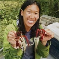 A smiling woman holds up a crawfish in each hand.