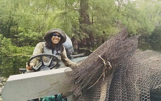 A woman in a hat steers a boat while holding a net.
