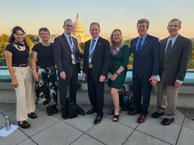 A group of TNC in Massachusetts staff and trustees standing on a balcony with the U.S. Capitol in the background at sunset.