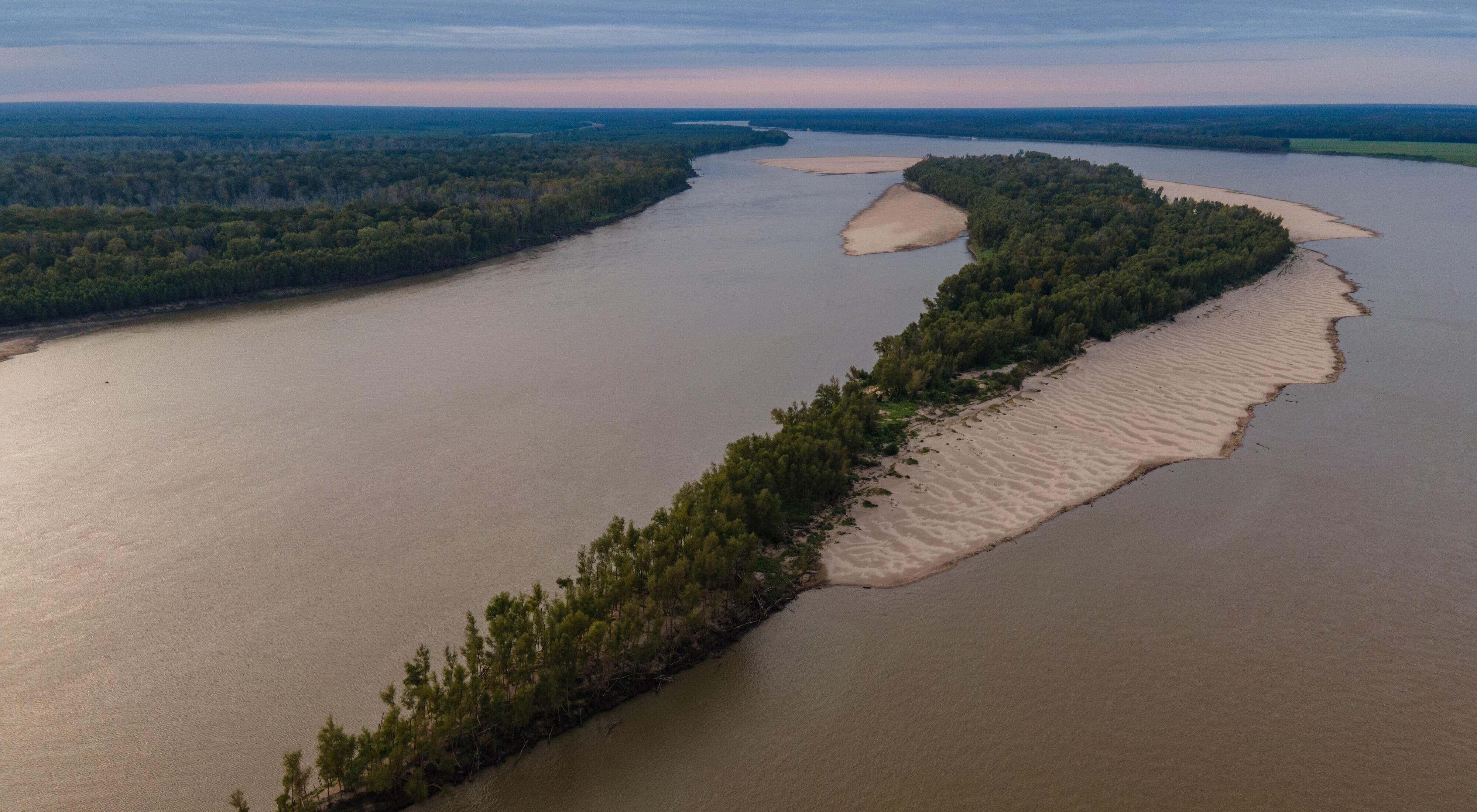 Aerial view of a long, narrow forested island in the middle of the wide Mississippi River.