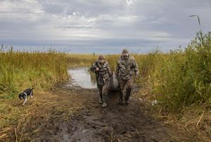 Two hunters dragging a boat out of a pond.