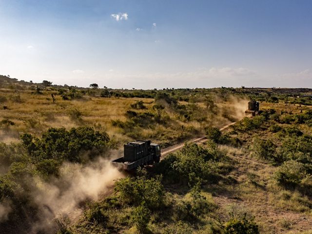 two large trucks driving through an African savannah.