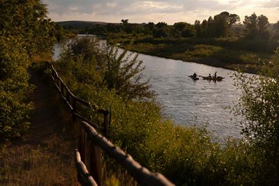 View of a river with several kayakers on it and green trees and vegetation around it during sunset.