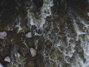Aeriel view of river water running over rocks with dark lighting.