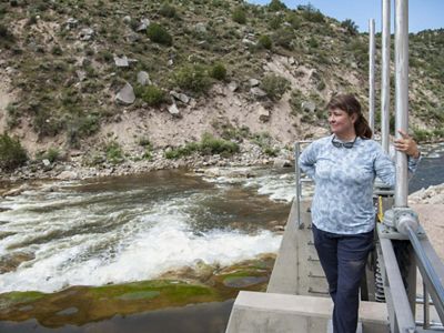 A woman stands on a platform and looks out at a rushing river.