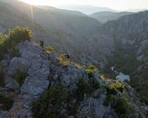 Hikers trek along a ridgeline above a limestone gorge with a river below.