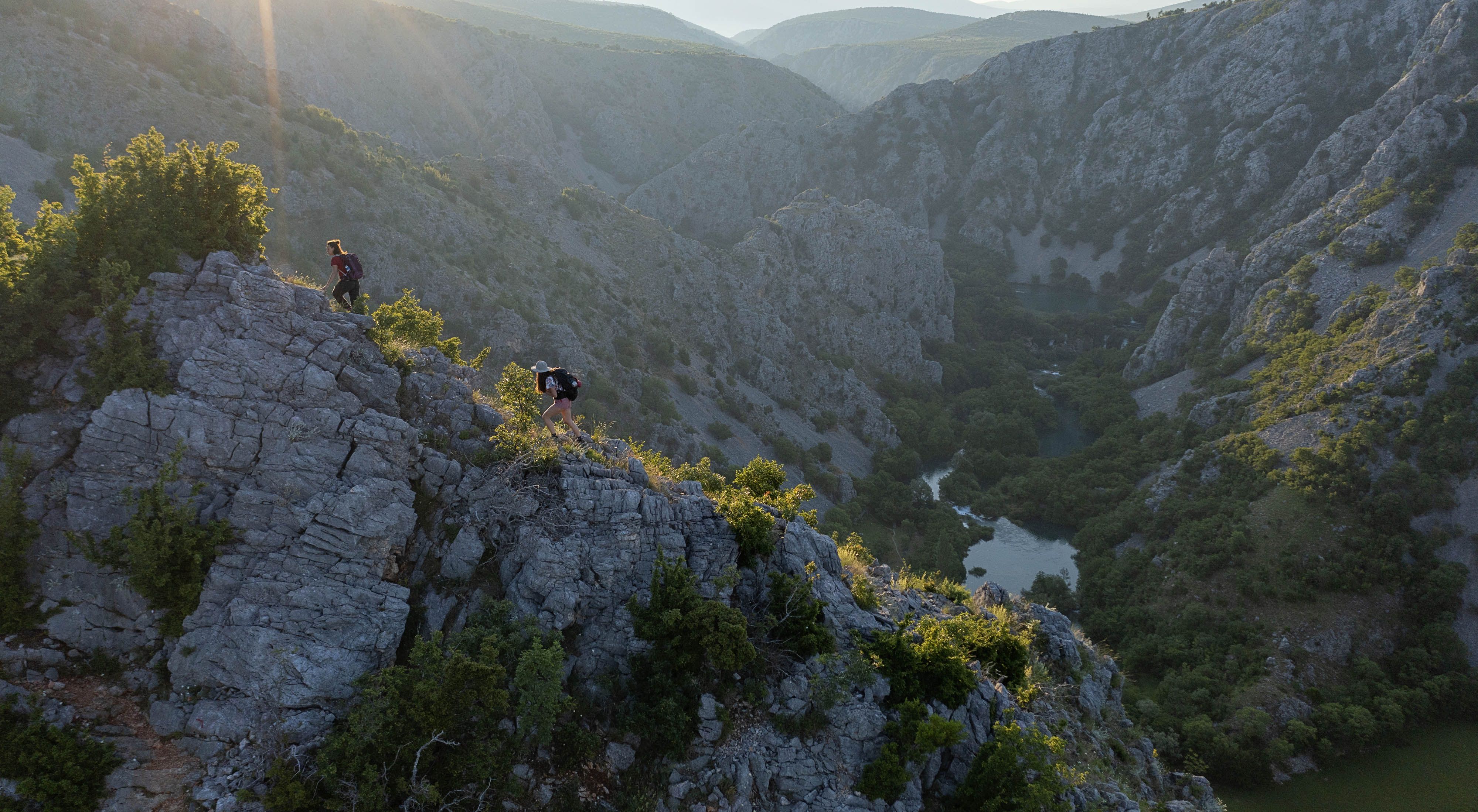 Hikers trek along a ridgeline above a limestone gorge with a river below.