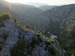 Hikers scale a steep ridge of rock overlooking a river valley.