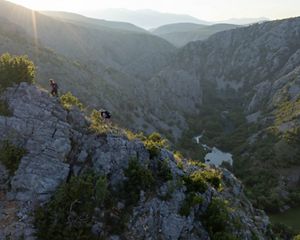 Hikers scale a steep ridge of rock overlooking a river valley.