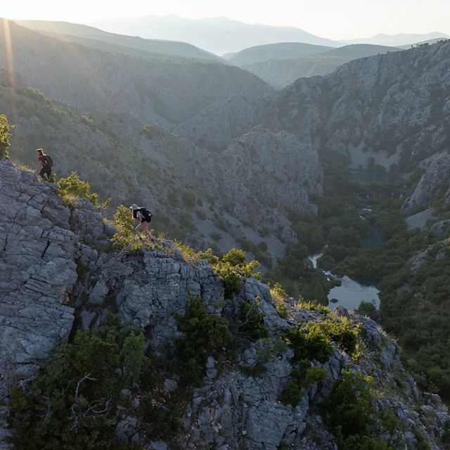 Hikers trek along a ridgeline above a limestone gorge with a river below.