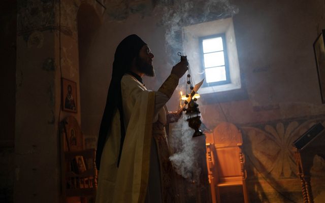 A monk holds a burning censer with a small window in the background.