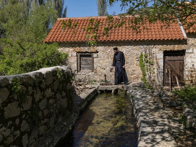 A monk walks outside a low stone building.