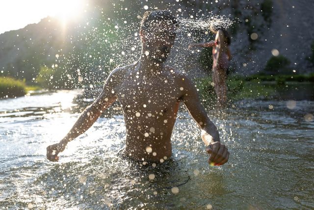 A man stands in a river, backlit by the sun, water droplets splashing all around him.