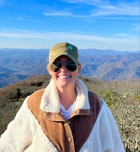 Candid headshot of Madeleine Gill taken in the mountains with rolling ridges behind her.