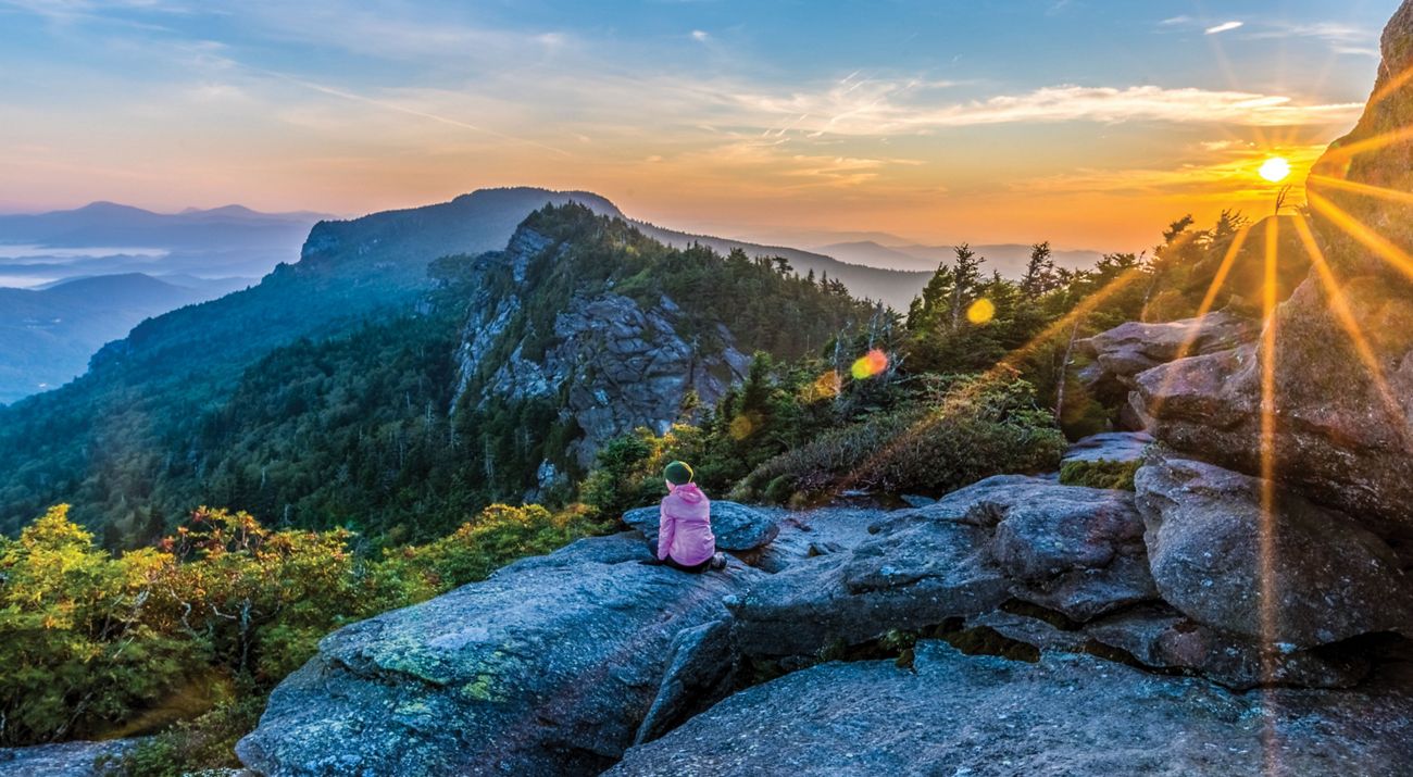 A seated woman wearing pink watching a mountain sunrise
