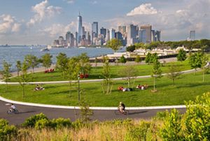 Landscape view of a city skyline in the distance, a large body of water to the left, and open, green city parks in the foreground. 