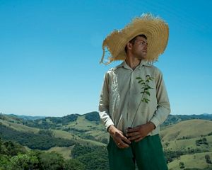 A person in a large straw hat holds a sapling ready to be planted. The Mantiqueria forest in Brazil is in the background.