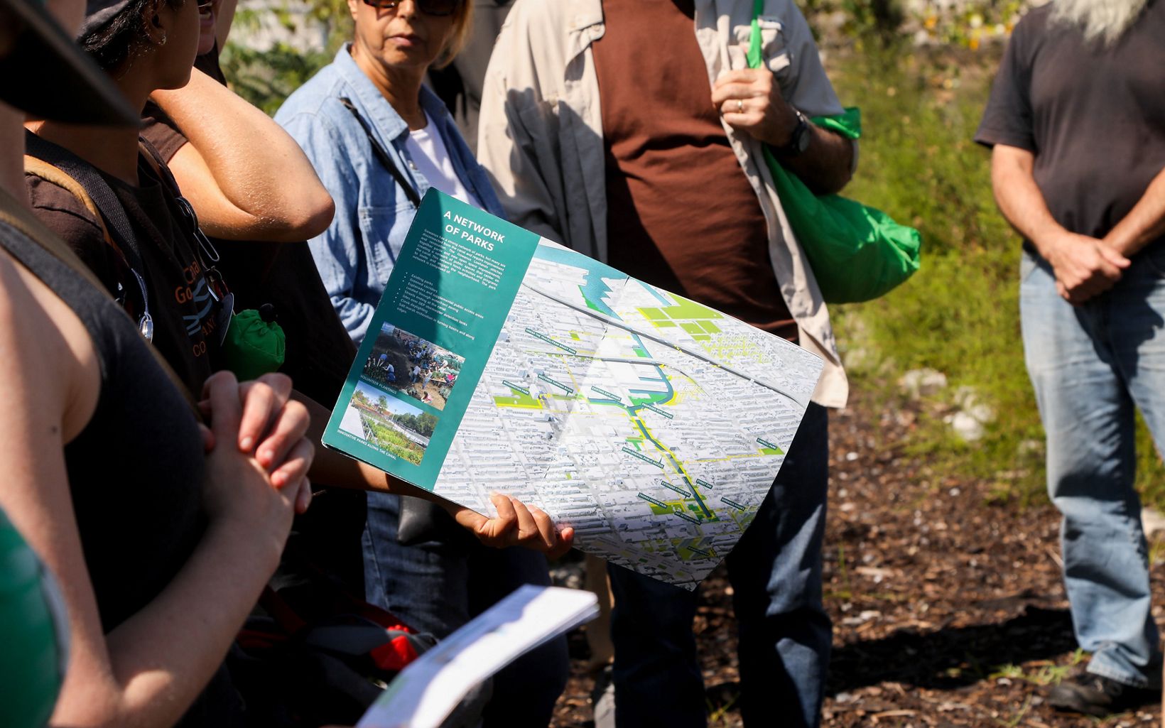 A volunteer holds a Gowanus Canal Conservancy map brochure with the words "A Network of Parks" written as the title of the map.
