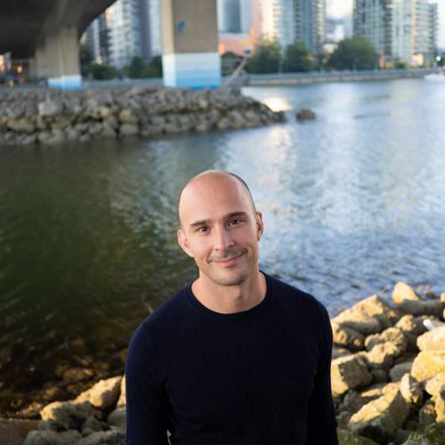 Person standing near water with a city behind.