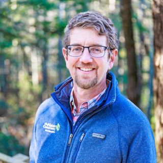 Un hombre con chaqueta azul se encuentra en el bosque.