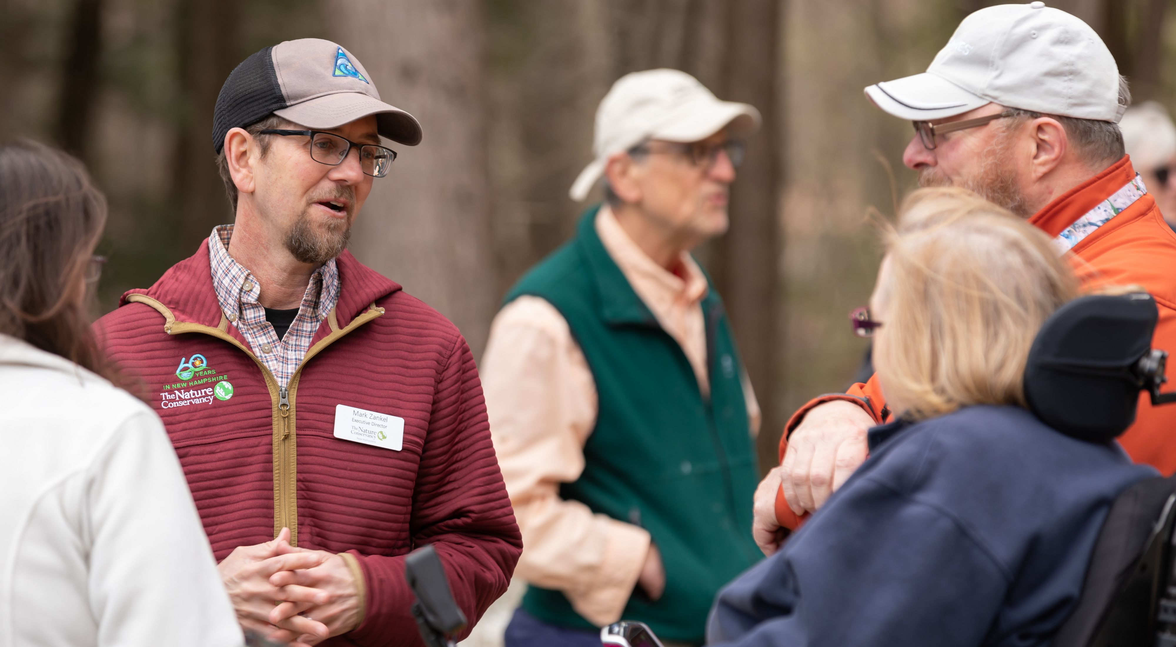 Mark Zankel speaks with a couple at a trailhead in the woods.