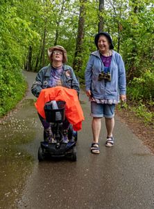 One person on a wheel chair and another person walking on a trail.