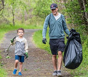 Father and son walking on a trail carrying a bag of trash.