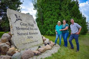 Three people people pose in front of a preserve entrance sign.