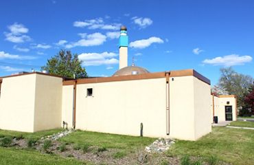 Back of the tan-painted Masjid An-Nur mosque building with bioswale (rain garden) in the foreground.