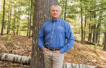 Deputy State Director Matt Dallman poses in front of a tree with a downed birch tree at his feet in an open Northwoods forest.