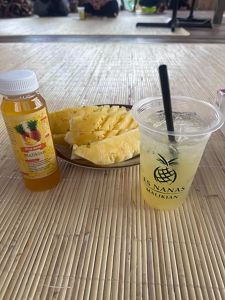 A bottle of pineapple syrup, a dish of fresh pineapple and a cup of pineapple juice sit arranged on a table.