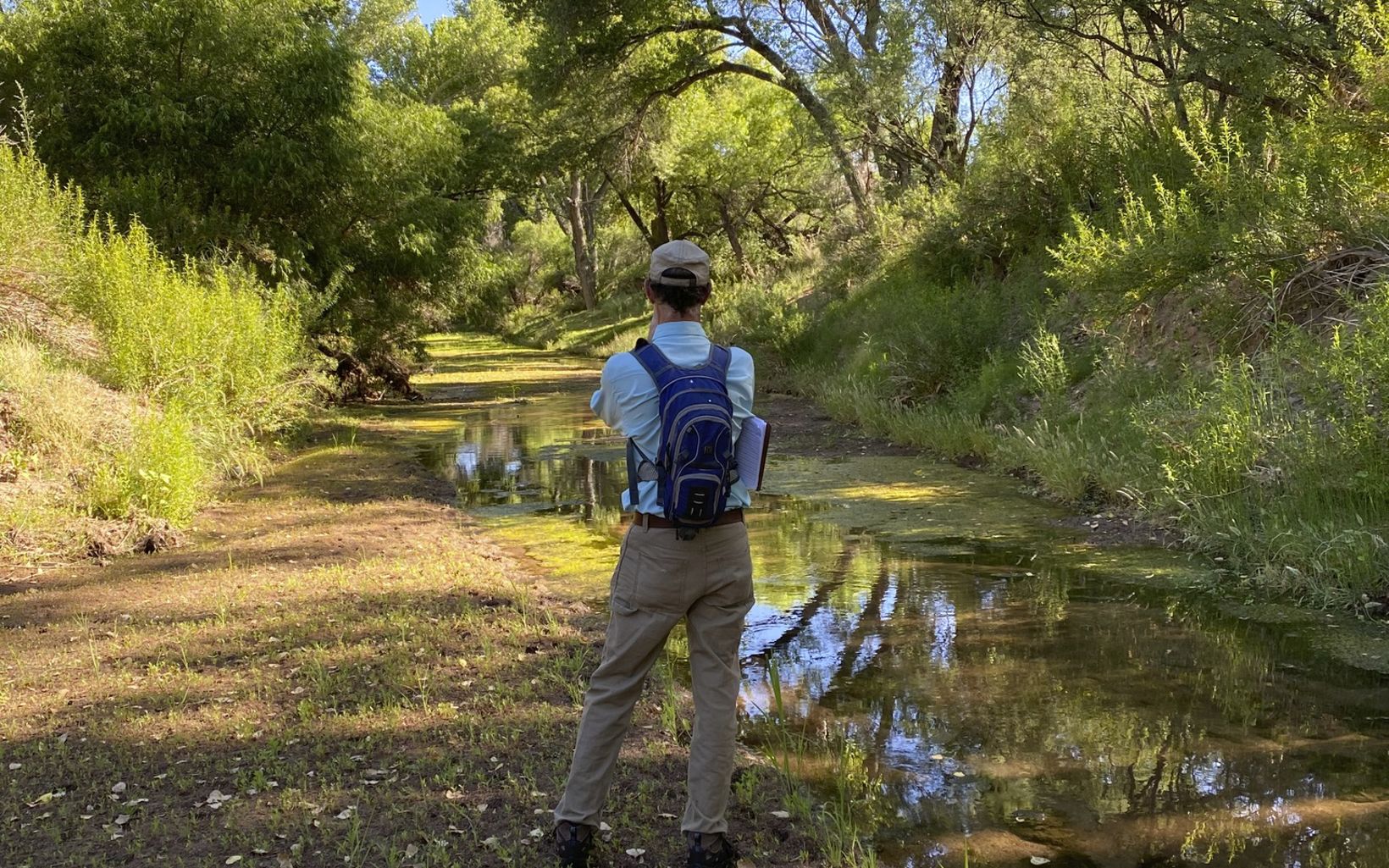 A mapping volunteer stands next to a river with his back to the camera and looks downstream.