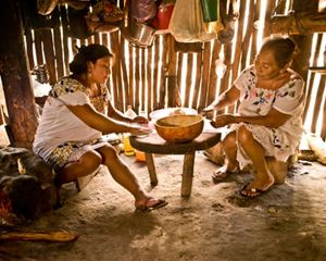 Two people prepare food on a simple table in a family cooking hut in the Maya Forest in Mexico.
