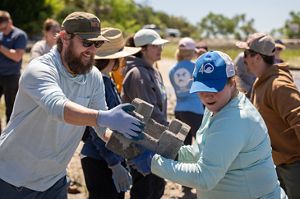 A smiling bearded man passes a concrete block to a woman with a blue 4Oceans hat.