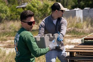 Two men pass a concrete block to each other. Both wear sunglasses.