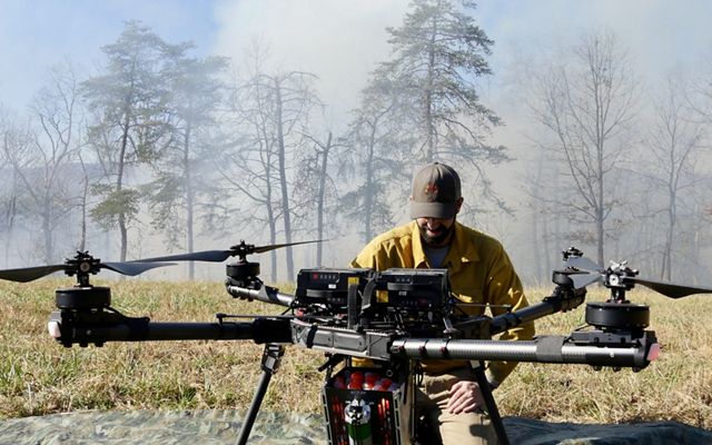 A man kneels next to a large fire ignition drone during a controlled burn in Maryland.