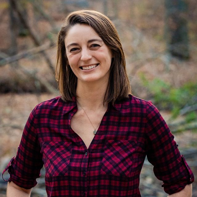 Casual headshot of Resilient Coasts Program Director Jackie Specht. A smiling woman stands on a forest trail with blurred trees visible behind her.